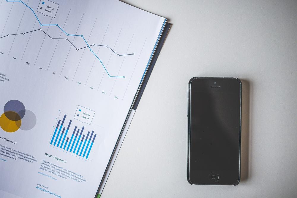 Un smartphone noir posé à côté d'un magazine ouvert contenant des graphiques et des statistiques.