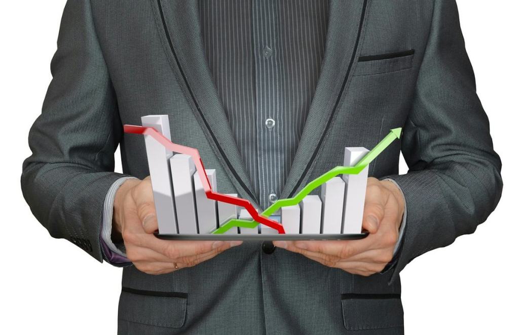 Homme en costume tenant une tablette avec des graphiques financiers, affichant une tendance à la baisse en rouge et une tendance à la hausse en vert.